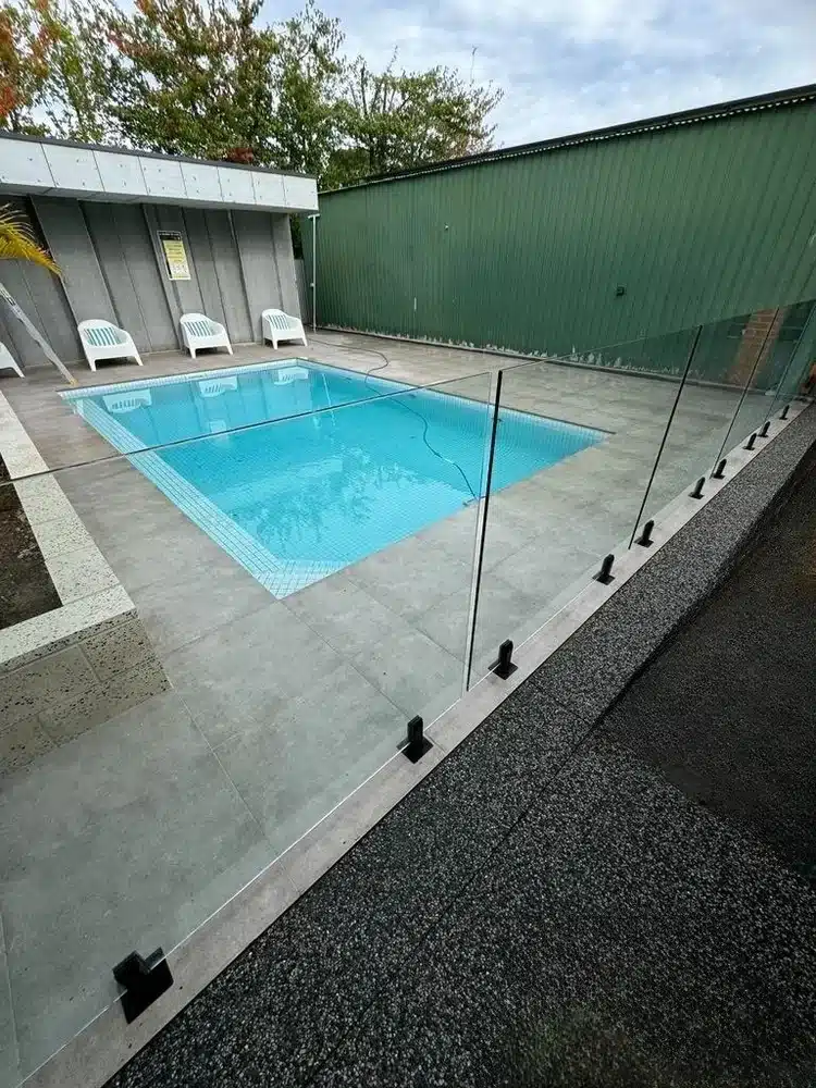 Concrete pool surround behind a glass pool fence